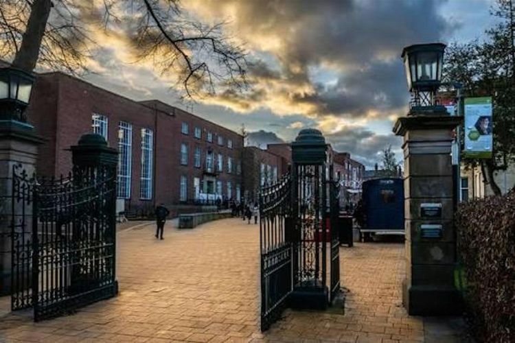The image the University of Leeds' Student Union and Woodhouse Building to the left through open metal gates, under a dark, wintry sky.