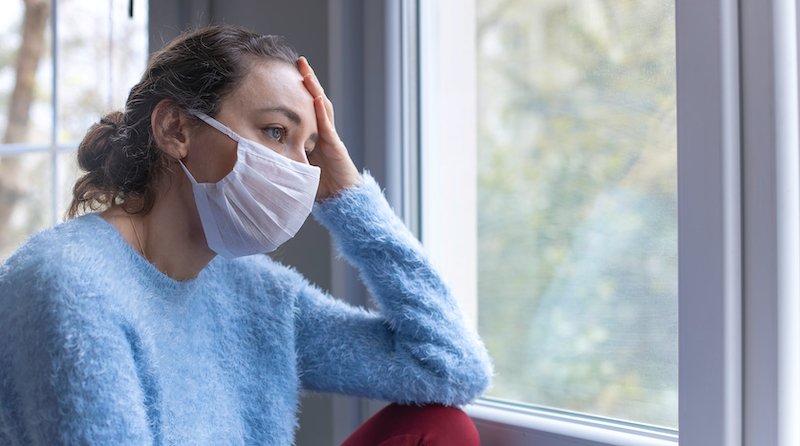 Person wearing a facemask looking out of a window