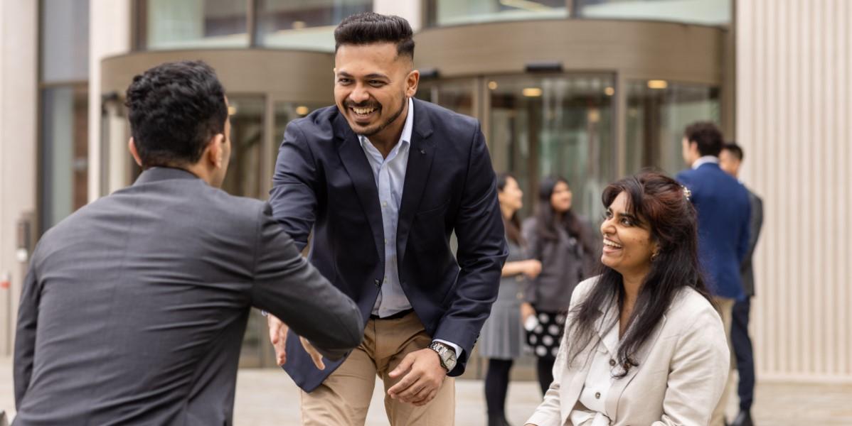 MBA students greeting by shaking hands outside a modern building.