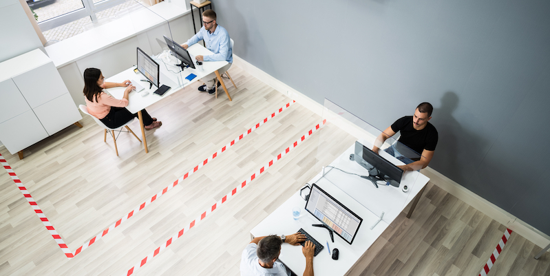 Four office workers sat apart at two desks with tape on the floor, marking out the distance