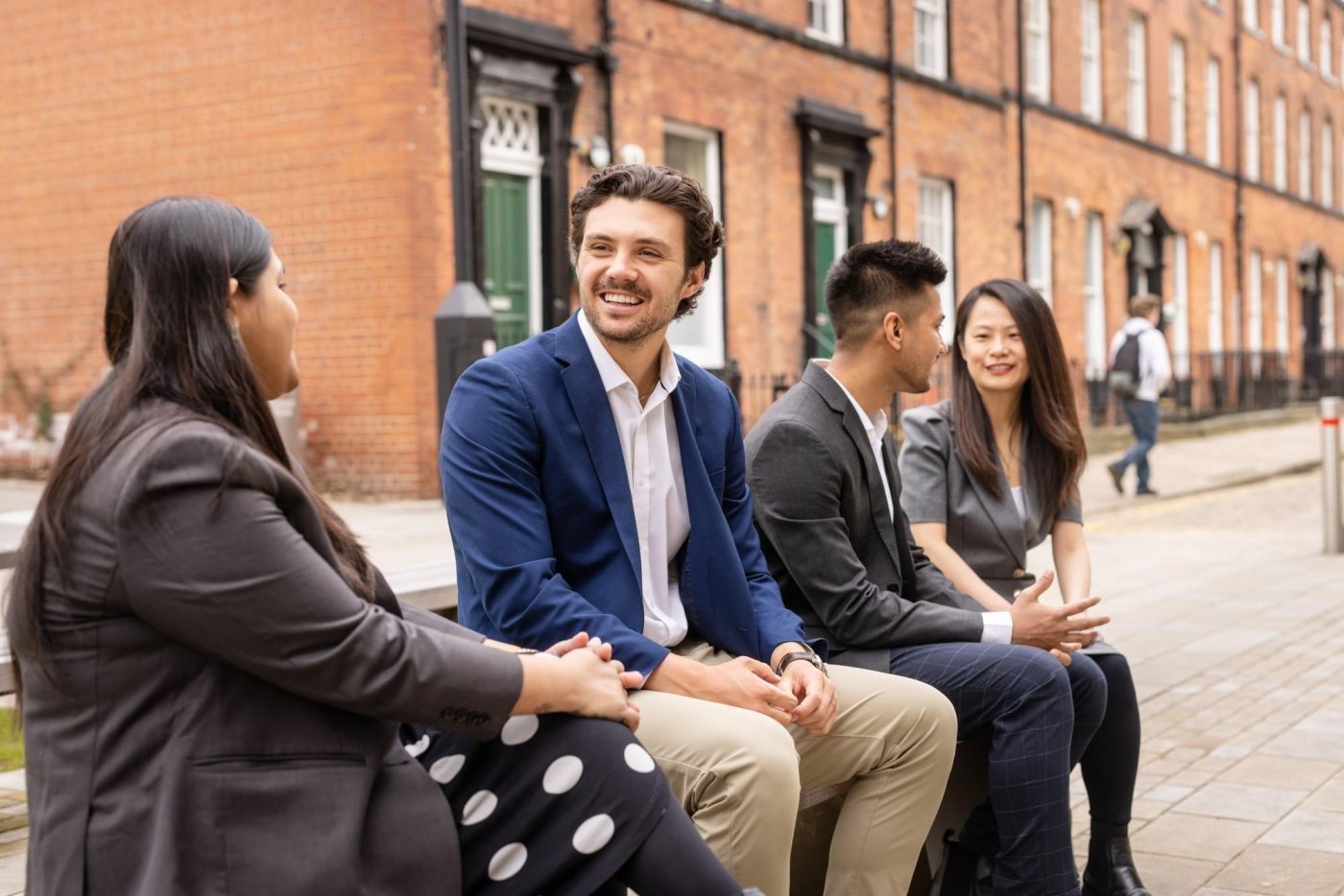 A group of MBA students sit on a bench in front of a red brick building.