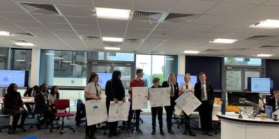photo of group of secondary school students holding up posters with innovation project ideas on them.