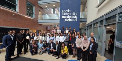 A group of students and professionals stood in front of a Leeds University Business School banner.