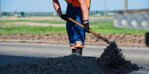 A highways worker using a tool to spread fresh asphalt across a road