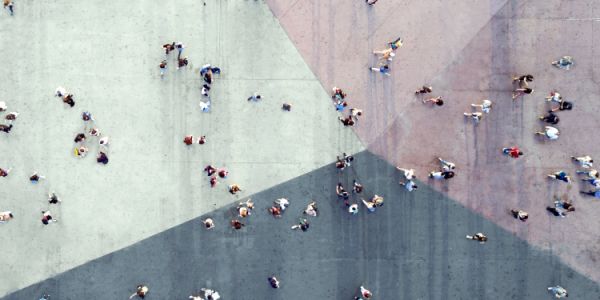 Aerial view of many people moving across an open plaza with intersecting geometric shapes in muted colours