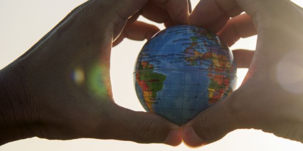 Hands, in a heart shape, holding a small globe