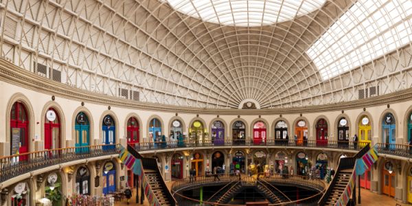 Interior of a circular shopping arcade - The Corn Exchange in Leeds - with colourful shopfronts beneath a glass-domed roof