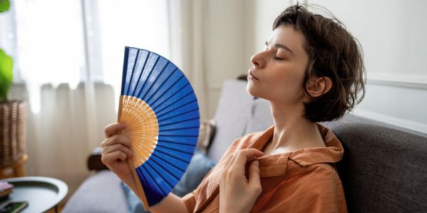 Woman struggling in the heat, sitting on a sofa and fanning herself with paper fan