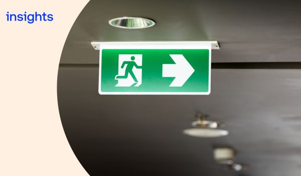 Green emergency exit sign hanging from a ceiling, with a cream curved overlay on the left with the word 
