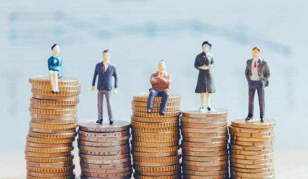 Small figurines of people standing or sitting on stacks of coins of varying heights, symbolising income inequality or differences in financial status