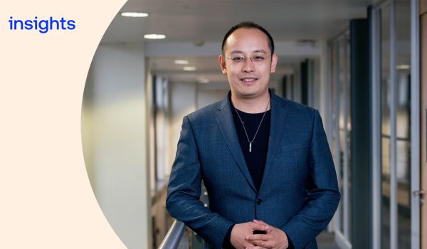 Jie Chen in an office corridor, smiling at the camera. There is a cream curve overlay with the word 