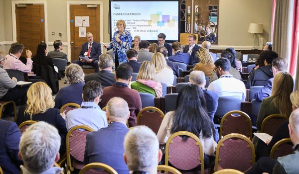 Shirley Cooper stood up with a microphone, as part of a panel discussion, speaking in front of a seated audience