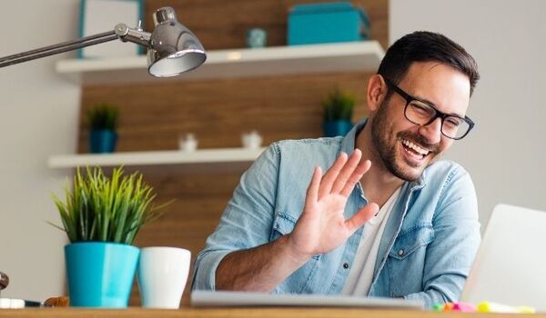 Person sat at desk, waving at laptop screen