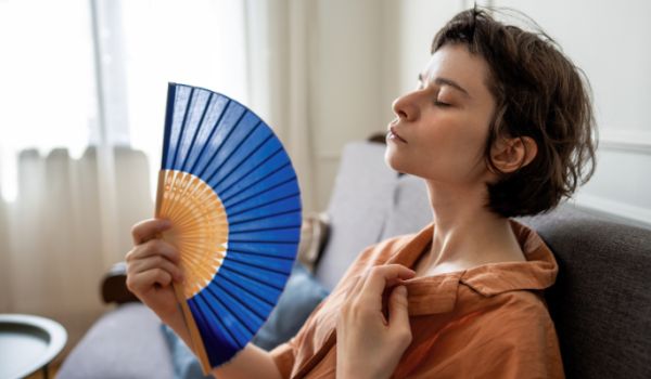 Woman struggling in the heat, sitting on a sofa and fanning herself with paper fan