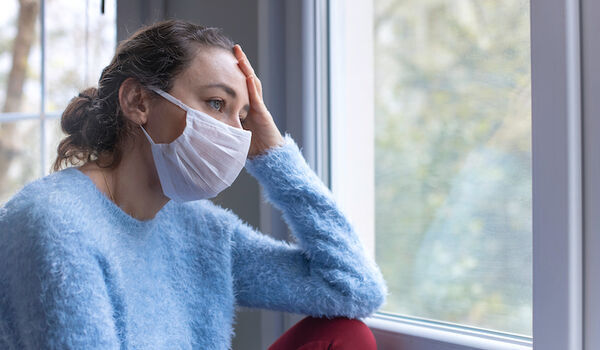 Person wearing a facemask looking out of a window