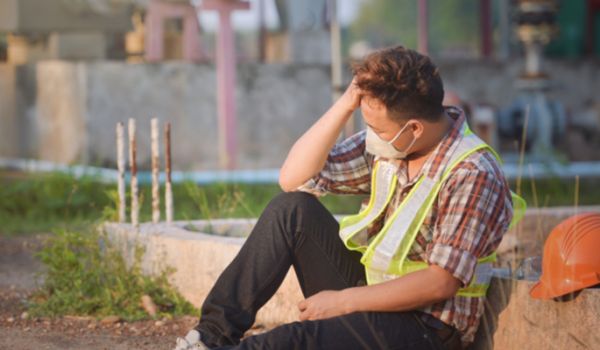 Construction worker sat outside on their own with head in hand