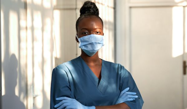 Health worker in scrubs and facemask stood in corridor