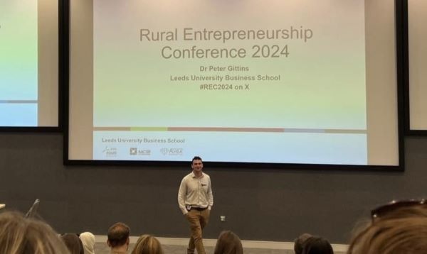 Peter Gittins presenting in front of an audience, stood in front of a screen with the words "Rural Entrepreneurship Conference 2024" on it.