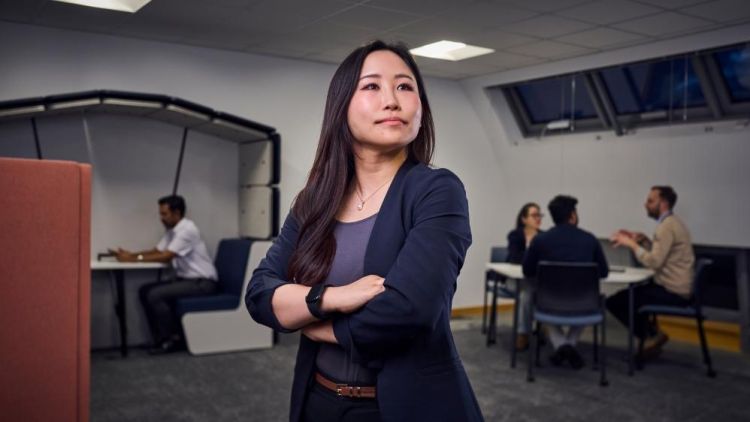 Woman standing in the middle of an office with arms folded looking confidently off camera