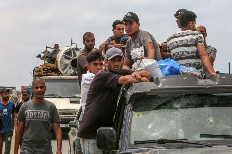 The image shows migrants with belongings atop a queue of vehicles as they attempt to flee their homes.