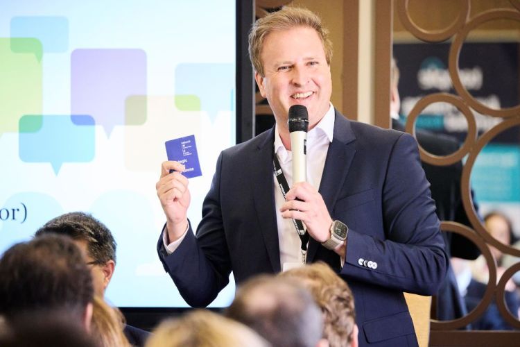 Simon Reid talking into a microphone and holding a booklet