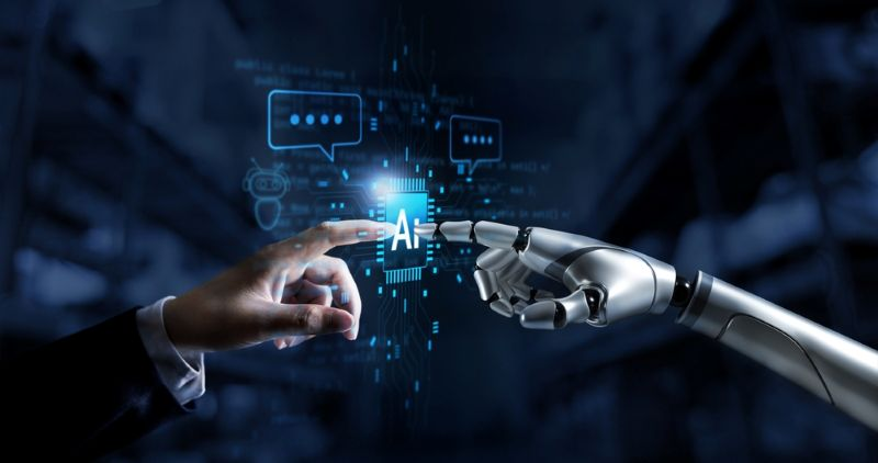 Human hand touching a transparent screen on one side, with a robotic hand touching the screen on the other. The screen says "AI" in the middle