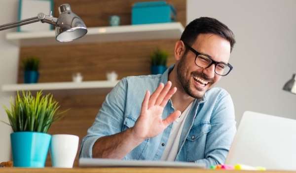 Person sat at desk, waving at laptop screen