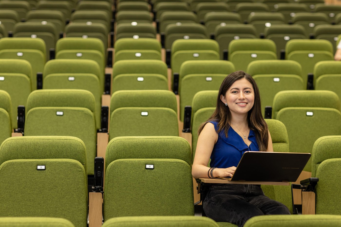 Student sitting at laptop in tiered lecture theatre with green seats.