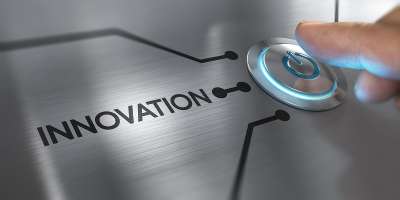 The picture shows the tip of a finger poised to press a button next to the word 'Innovation' on a metal contraption.