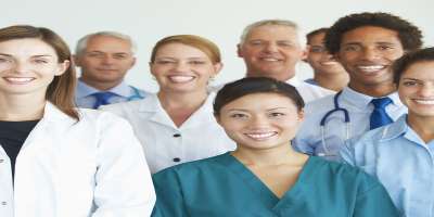 The image displays healthcare staff of minority ethnic backgrounds smiling at the camera.
