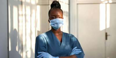 Health worker in scrubs and facemask stood in corridor